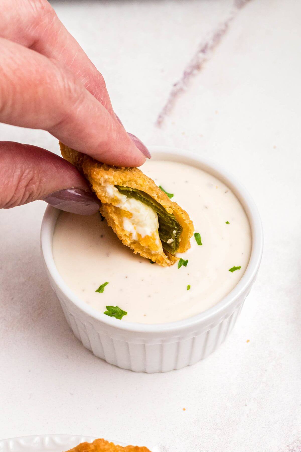 Golden crispy breaded jalapeno popper being dipped into ranch dressing. 