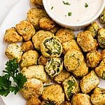 Golden breaded okra stacked on a white plate with a small dish or ranch dressing for dipping