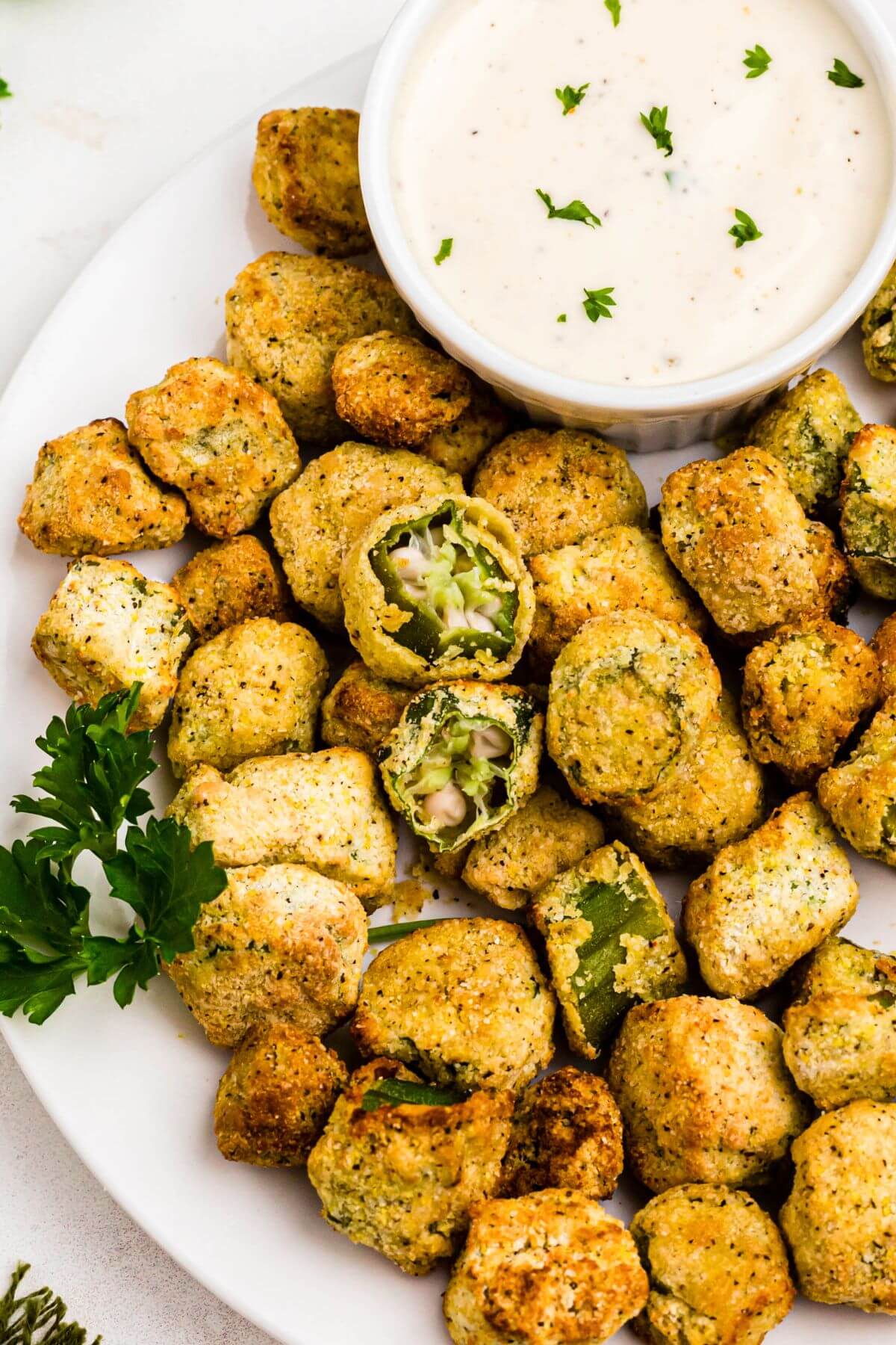 Golden brown breaded fried okra on a white plate with ranch dressing dipping sauce. 