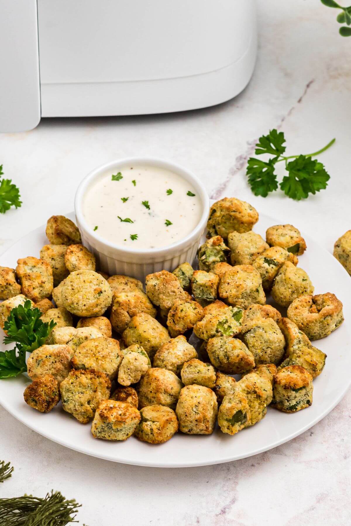 Golden breaded fried okra on a white plate in front of an air fryer 