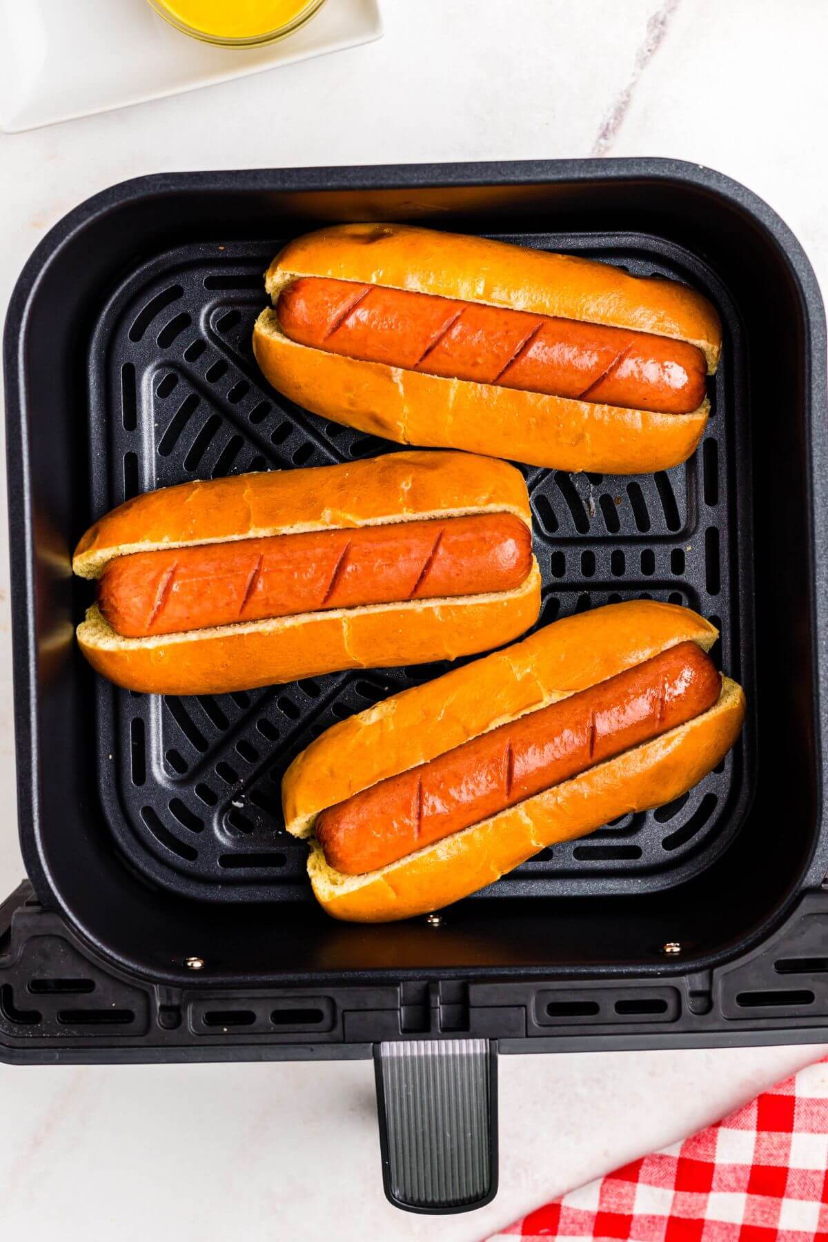 Golden juicy hot dogs in buns in the air fryer basket. 