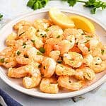 Orange shrimp stacked on a white plate with lemon wedges.