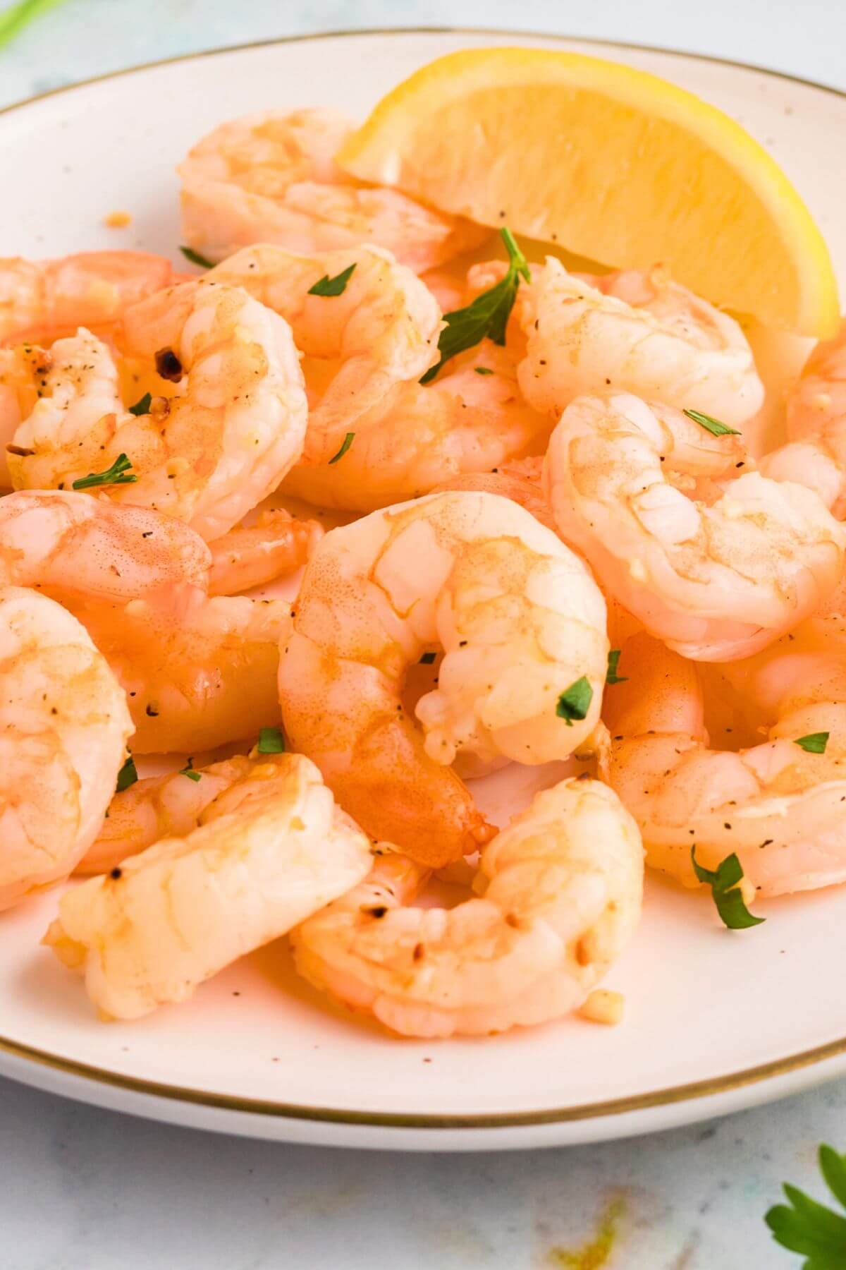 Orange juicy shrimp stacked on a white plate with a lemon wedge. 