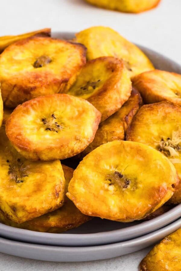 Golden plantain slices on a small plate in front of the air fryer.