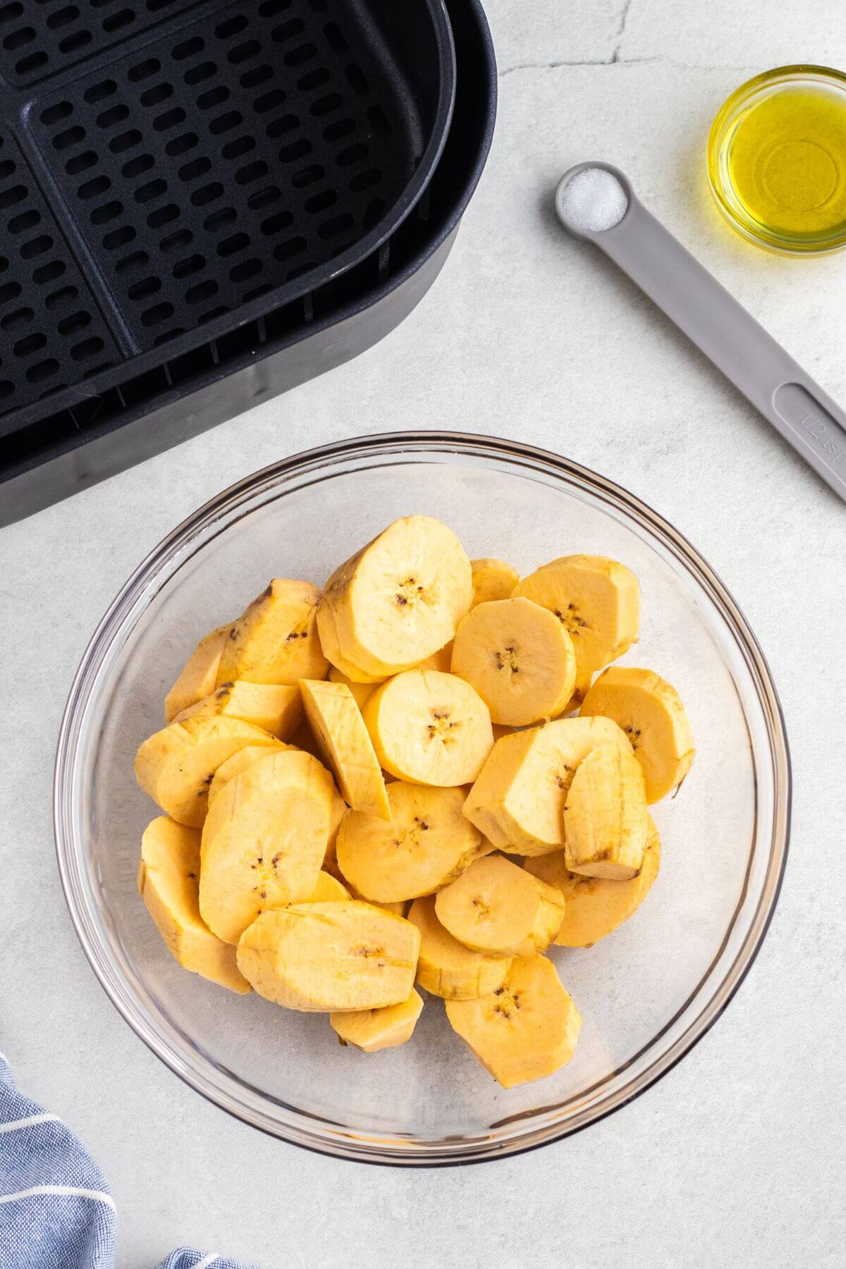 Slices of plantains in a clear glass bowl after being tossed with olive oil