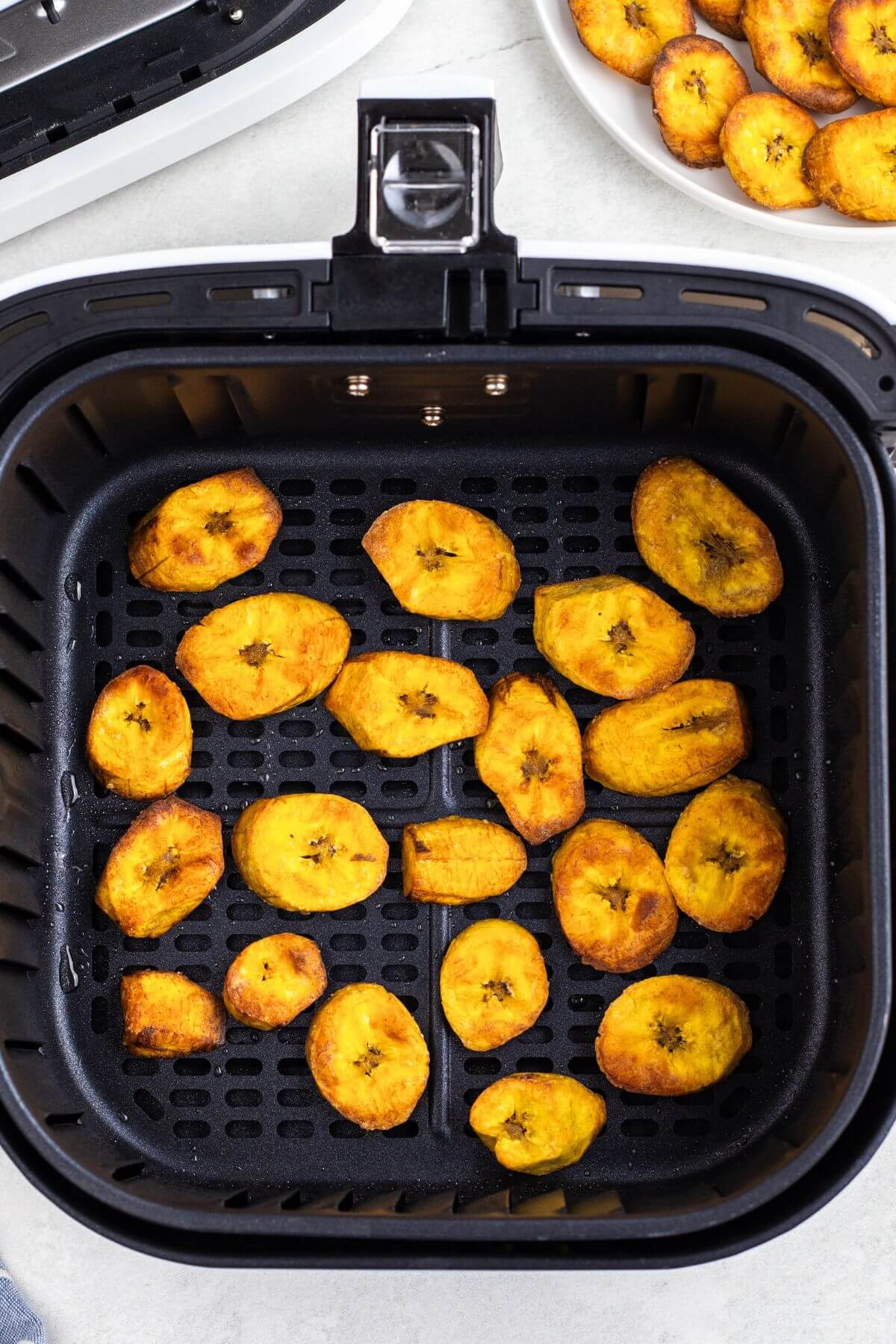 Golden brown plantain slices in the air fryer basket after being cooked. 
