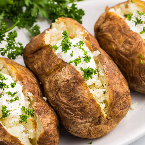 Air fryer Reheated baked potato on a plate with sour cream and fresh parsley.