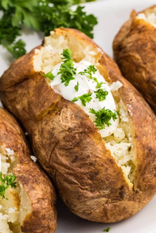 Air fryer Reheated baked potato on a plate with sour cream and fresh parsley.