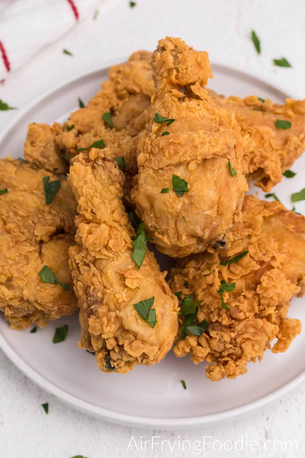 Fried chicken on a white plate topped with fresh chopped parsley that was reheated in the air fryer. 