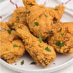 Fried chicken on a white plate that was reheated in the air fryer and garnished with fresh parsley.
