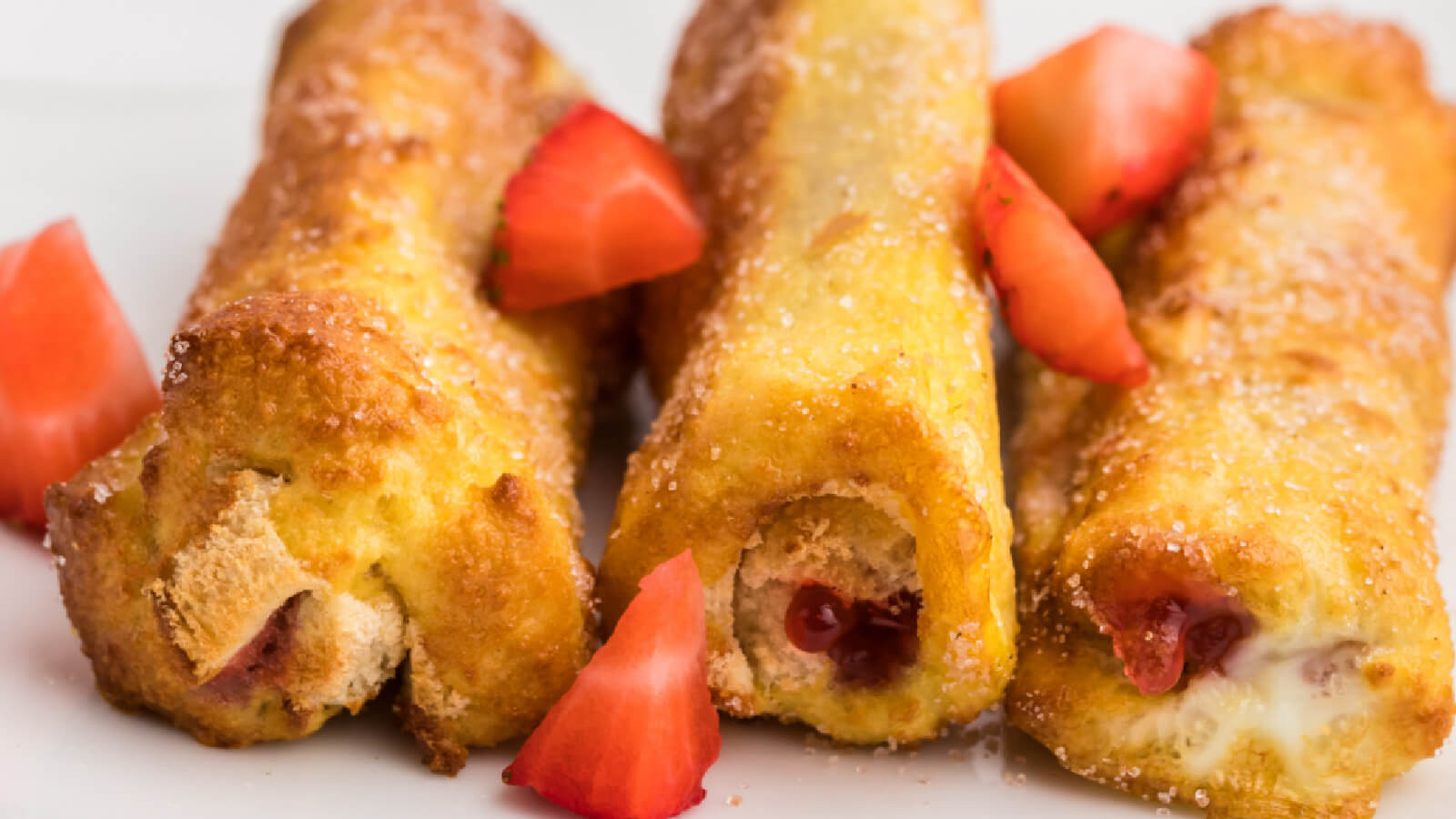 Close up photo of air fryer french toast roll ups with sliced strawberries on the side. 