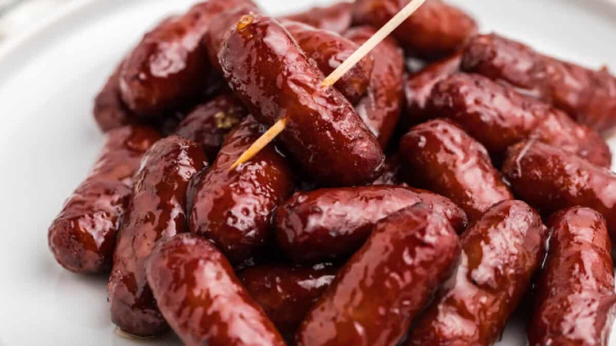 BBQ lil smokies on a white plate, a toothpick inserted through the top of one.