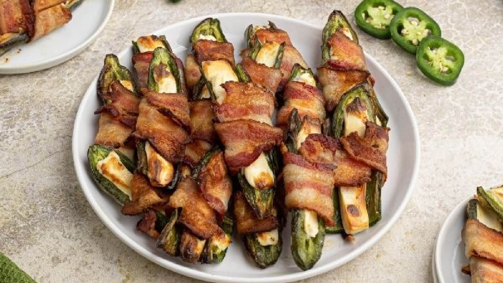 Jalapeno poppers on a white plate with sliced jalapenos on the side.
