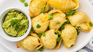 Taco stuffed shells on a serving tray with a side of guacamole in a small bowl.