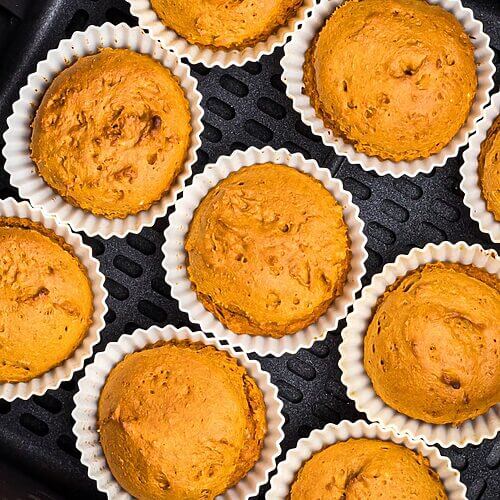 Moist orange pumpkin muffins in silicone liners in the air fryer basket.