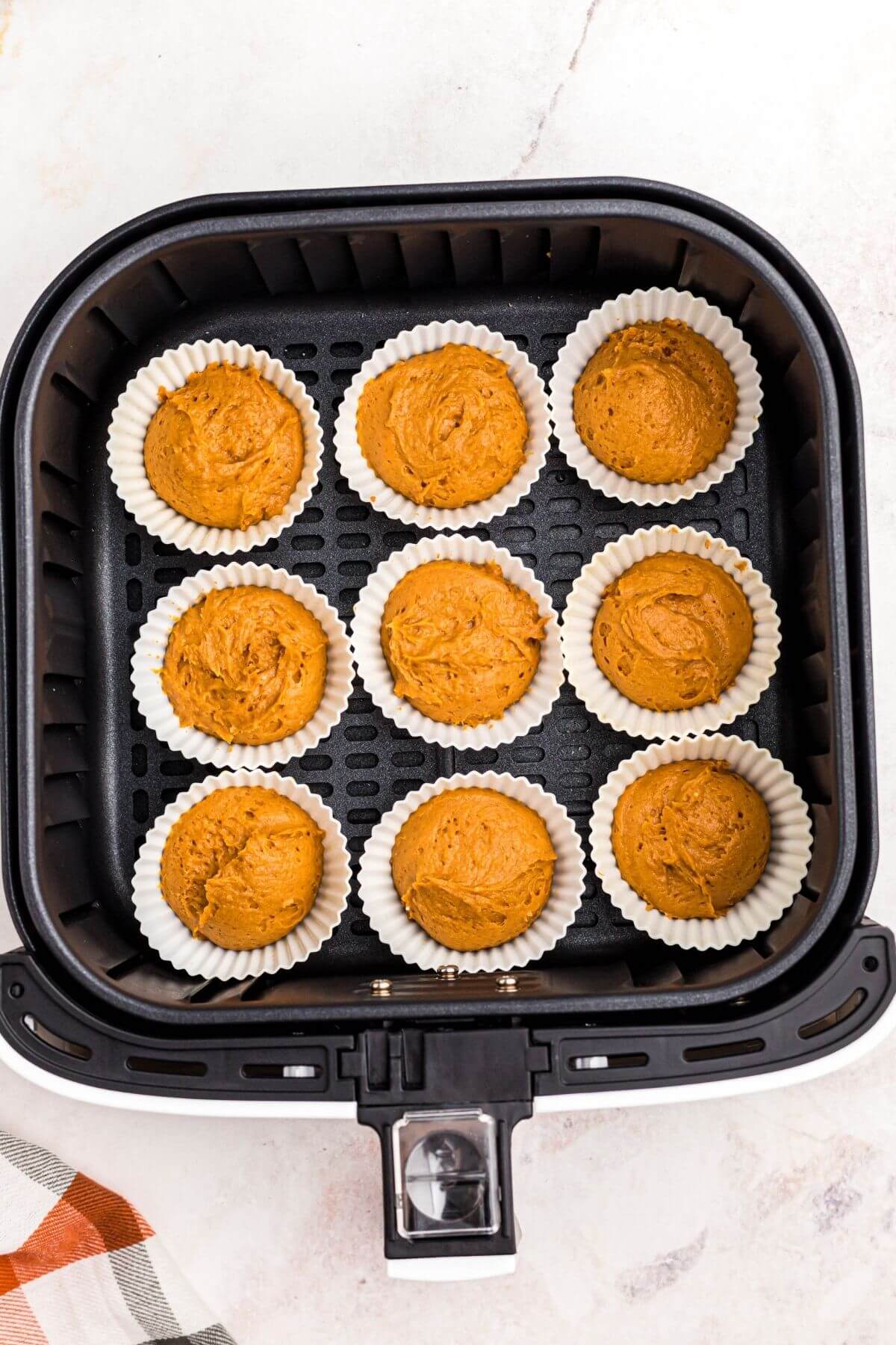 Uncooked muffin batter in silicone liners, in the air fryer basket. 