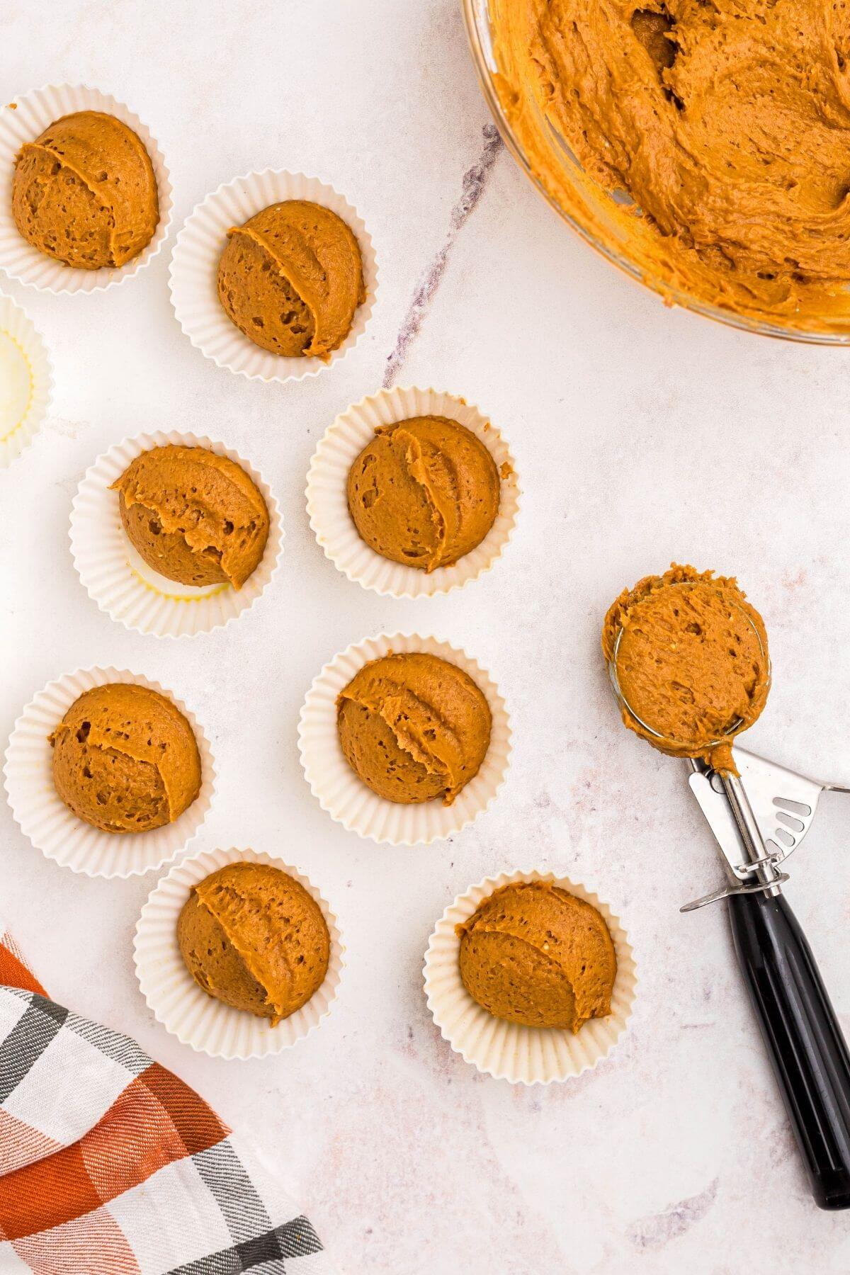Pumpkin muffin batter scooped out and place into silicone muffin liners, on a white marble table 