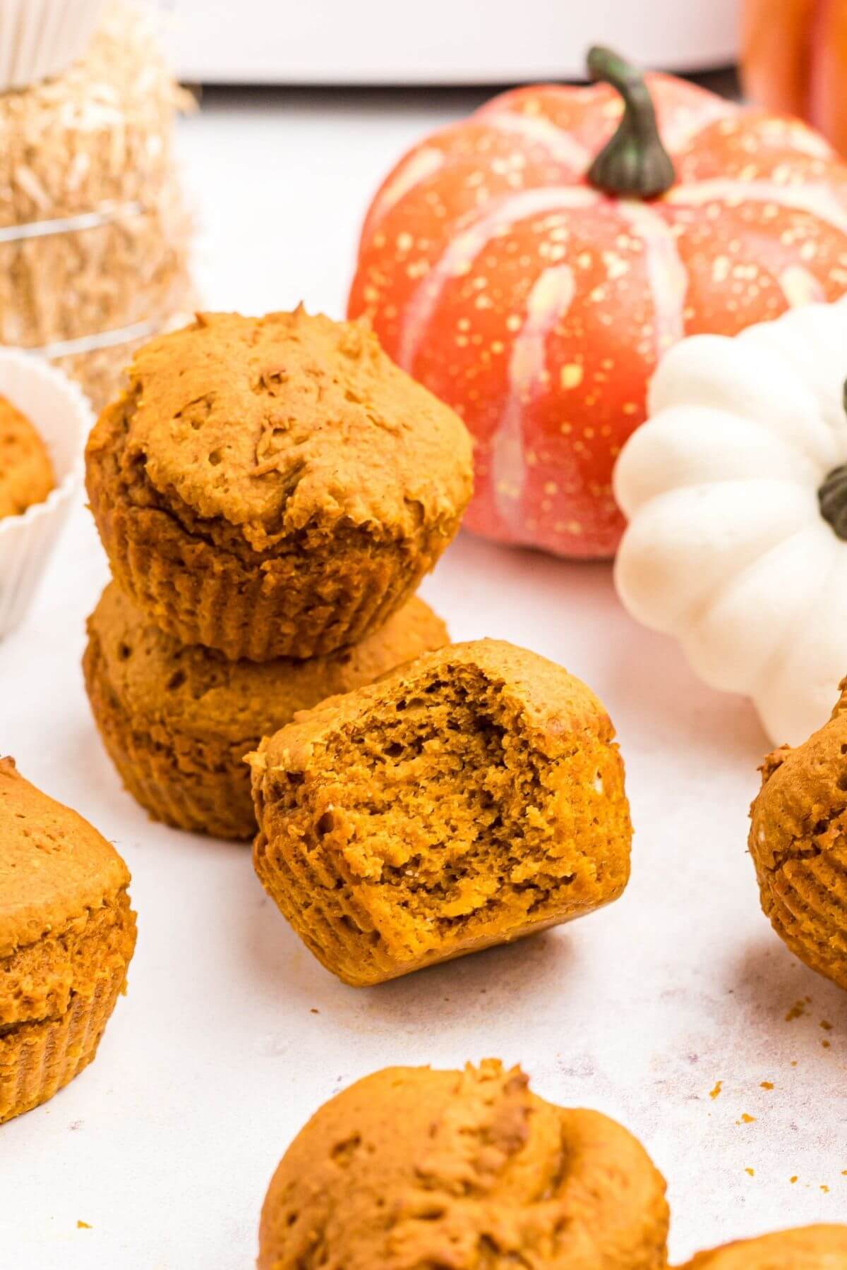 Moist pumpkin muffins stacked on top of each other with one muffin in front with a bite missing. 