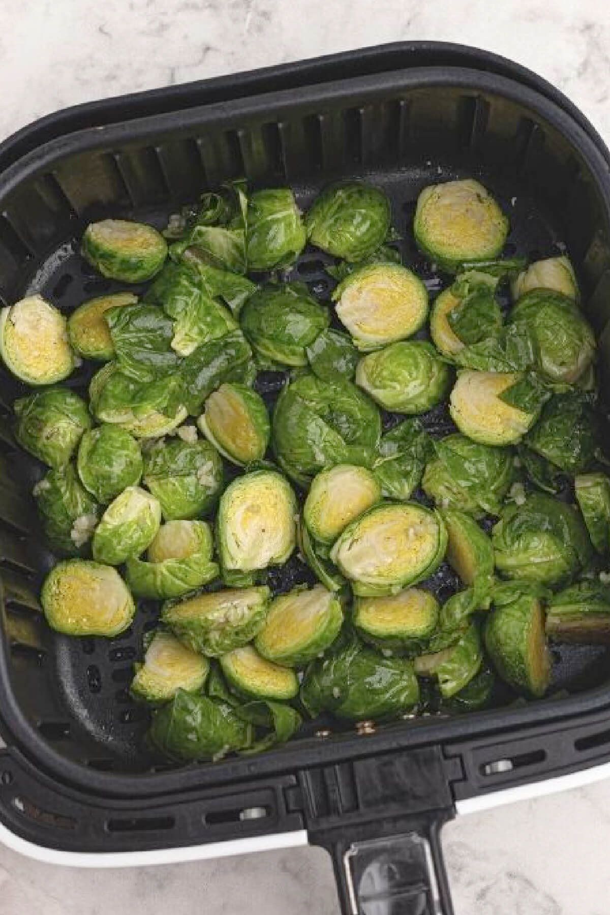 Prepared Brussels sprouts in the basket of the air fryer, ready to be cooked.