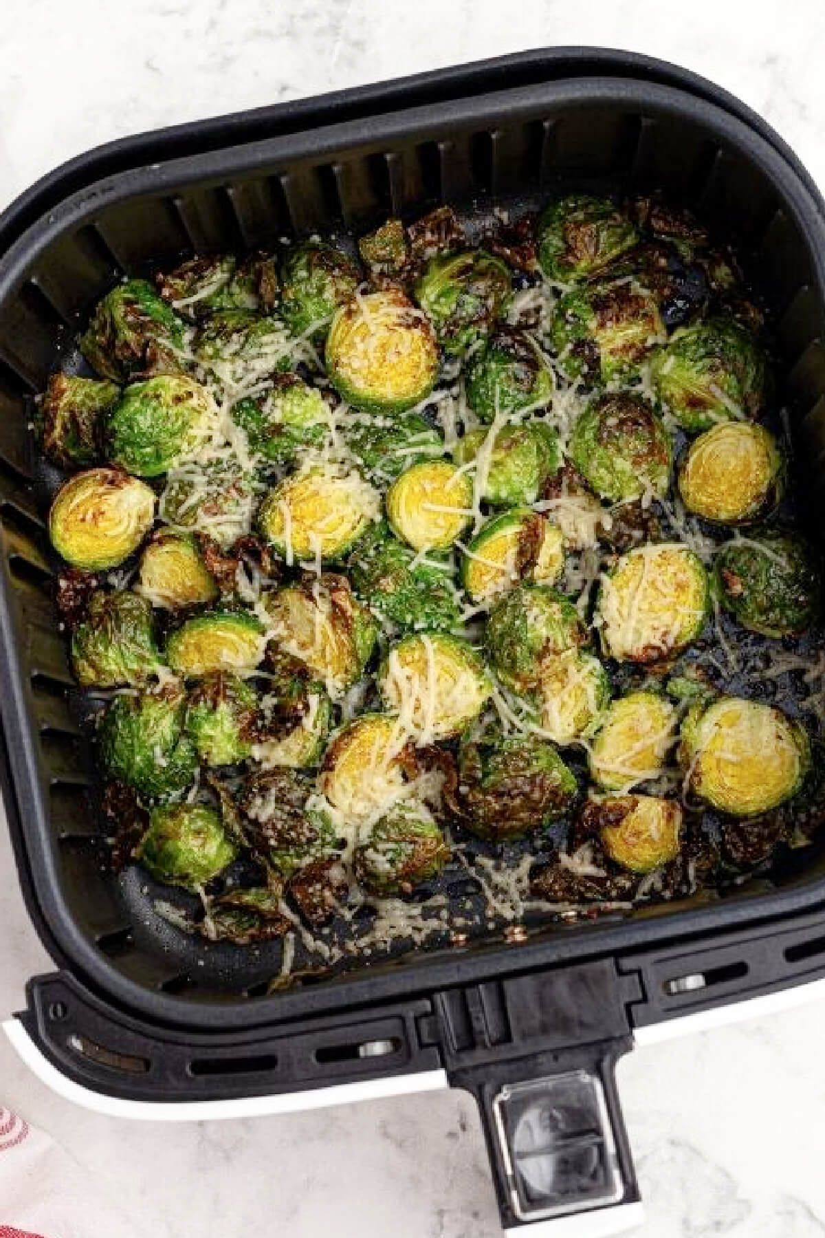 Brussels sprouts air fried and topped with parmesan cheese in the basekt of the air fryer.