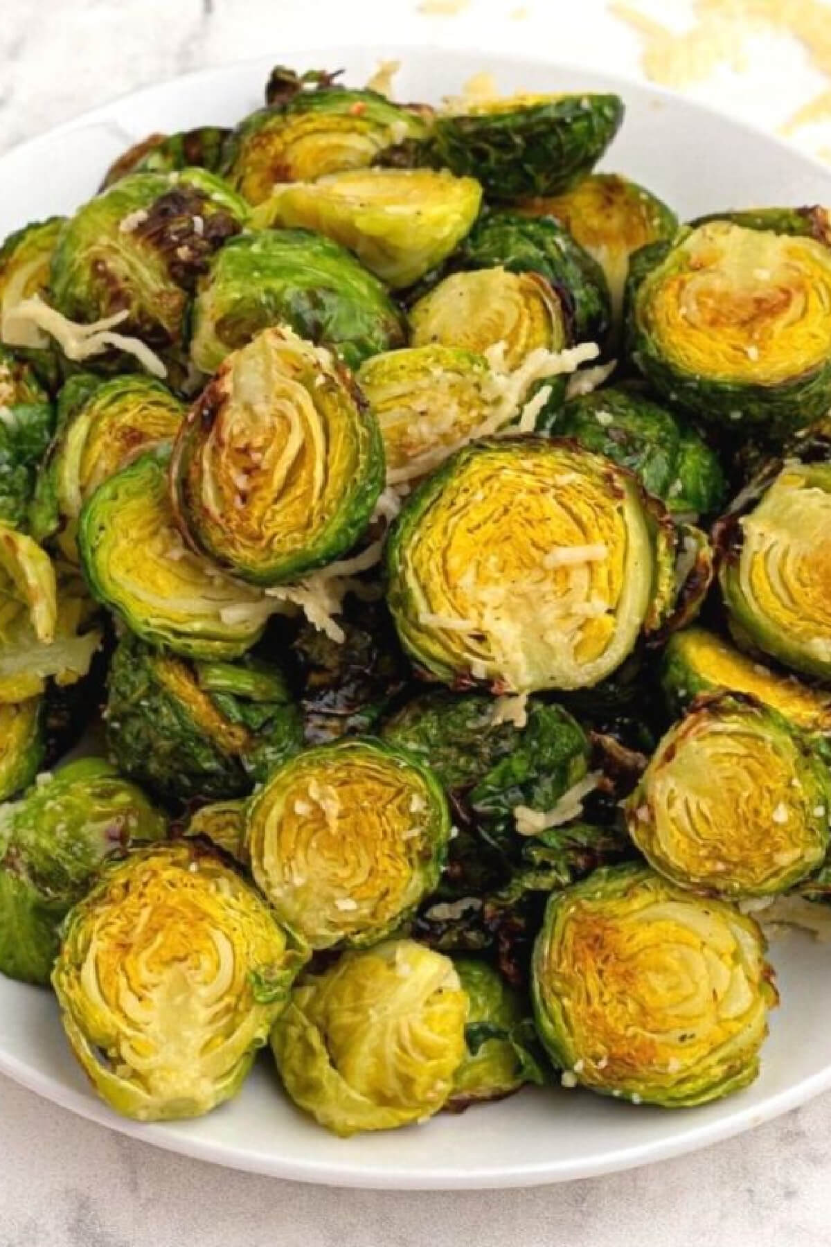 Close up of brussels sprouts on a white plate and topped with parmesan cheese. 