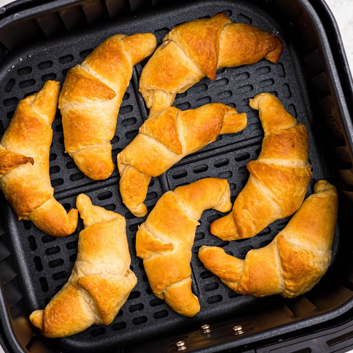 Golden crescent rolls in the air fryer basket after being cooked.
