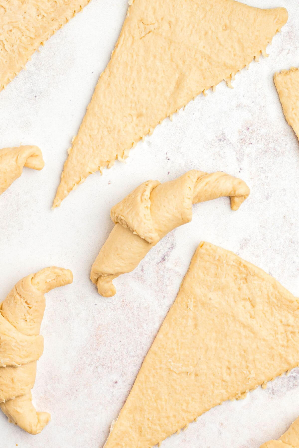 Uncooked crescent roll rolled out on a table into triangles with some rolled in crescent shapes. 