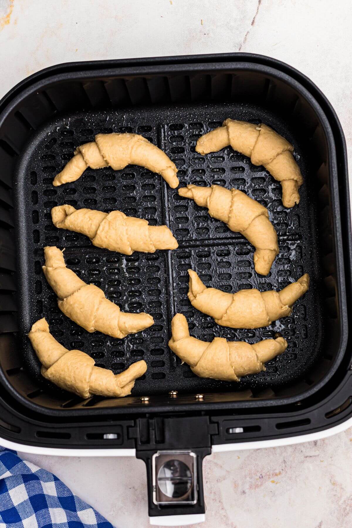 Uncooked rolled crescent rolls in the air fryer basket before being cooked. 