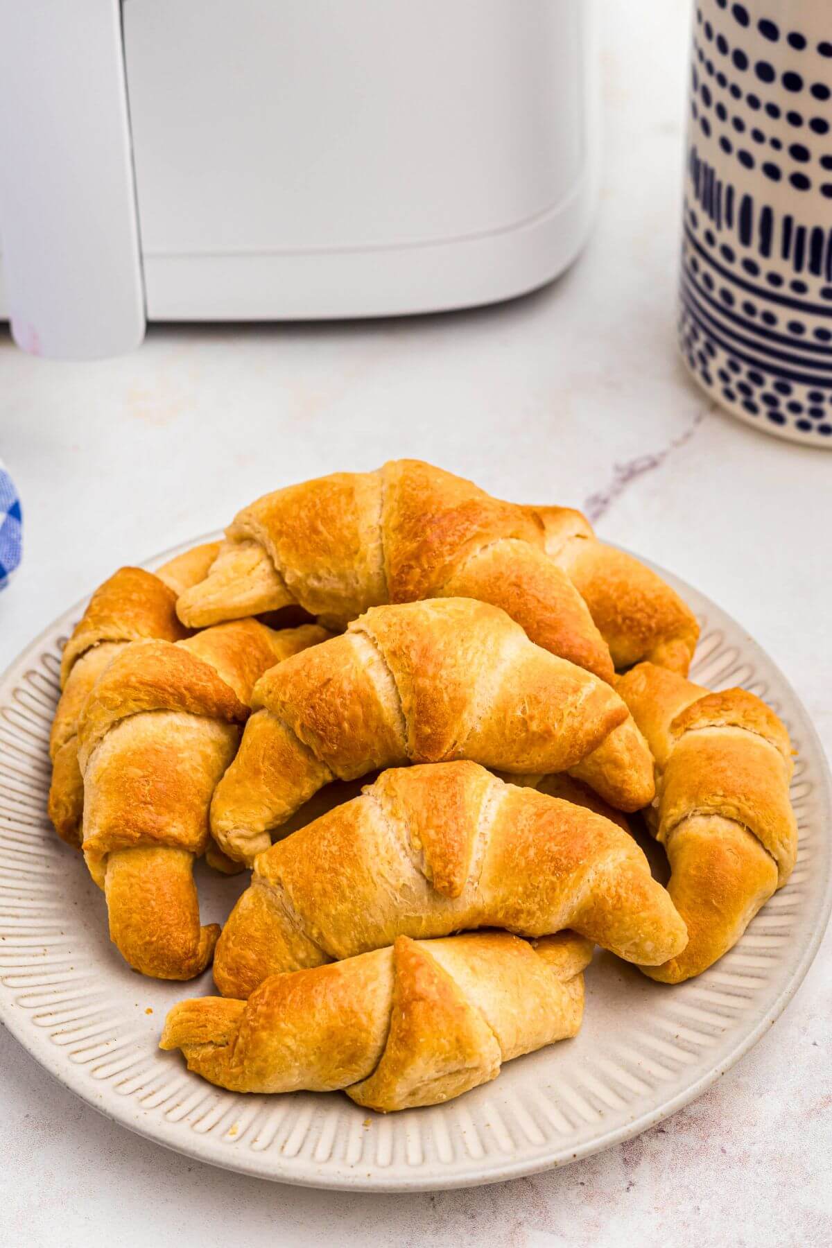 Golden flaky crescent rolls on a white plate in front of an air fryer. 