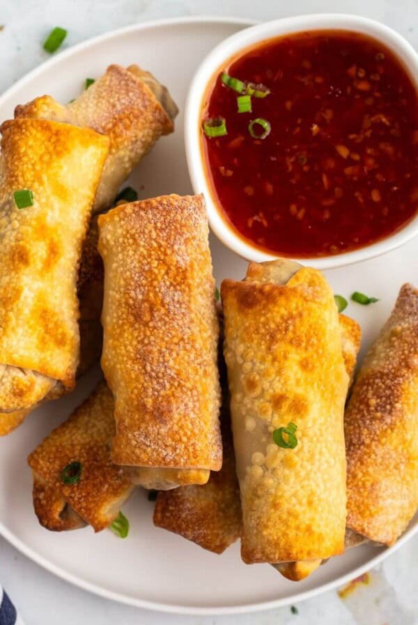 Golden crispy egg rolls on a white plate with cocktail sauce.