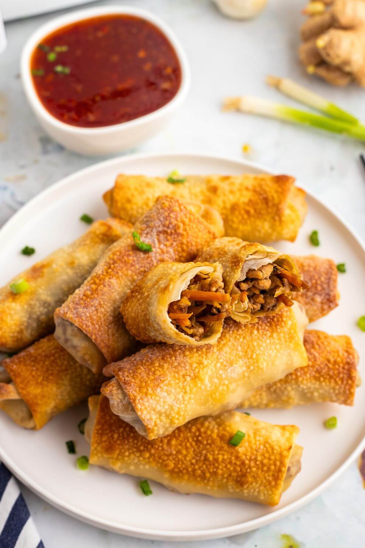 Golden brown pork and veggie stuffed egg rolls stacked on a white plate. 