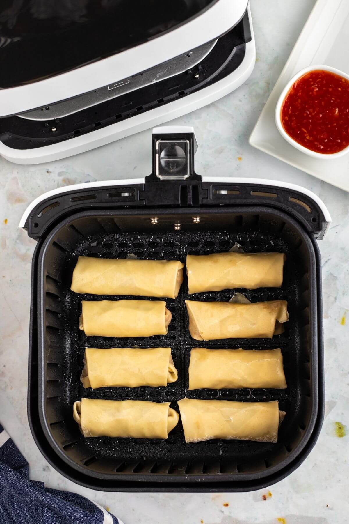 Uncooked rolled egg rolls in the air fryer basket. 