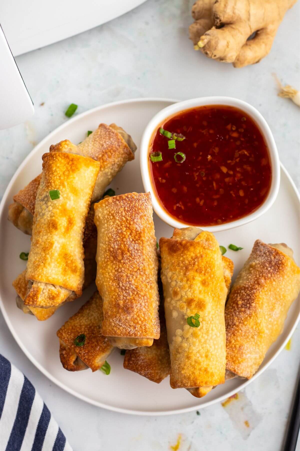 Golden crispy egg rolls on a white plate with cocktail sauce.