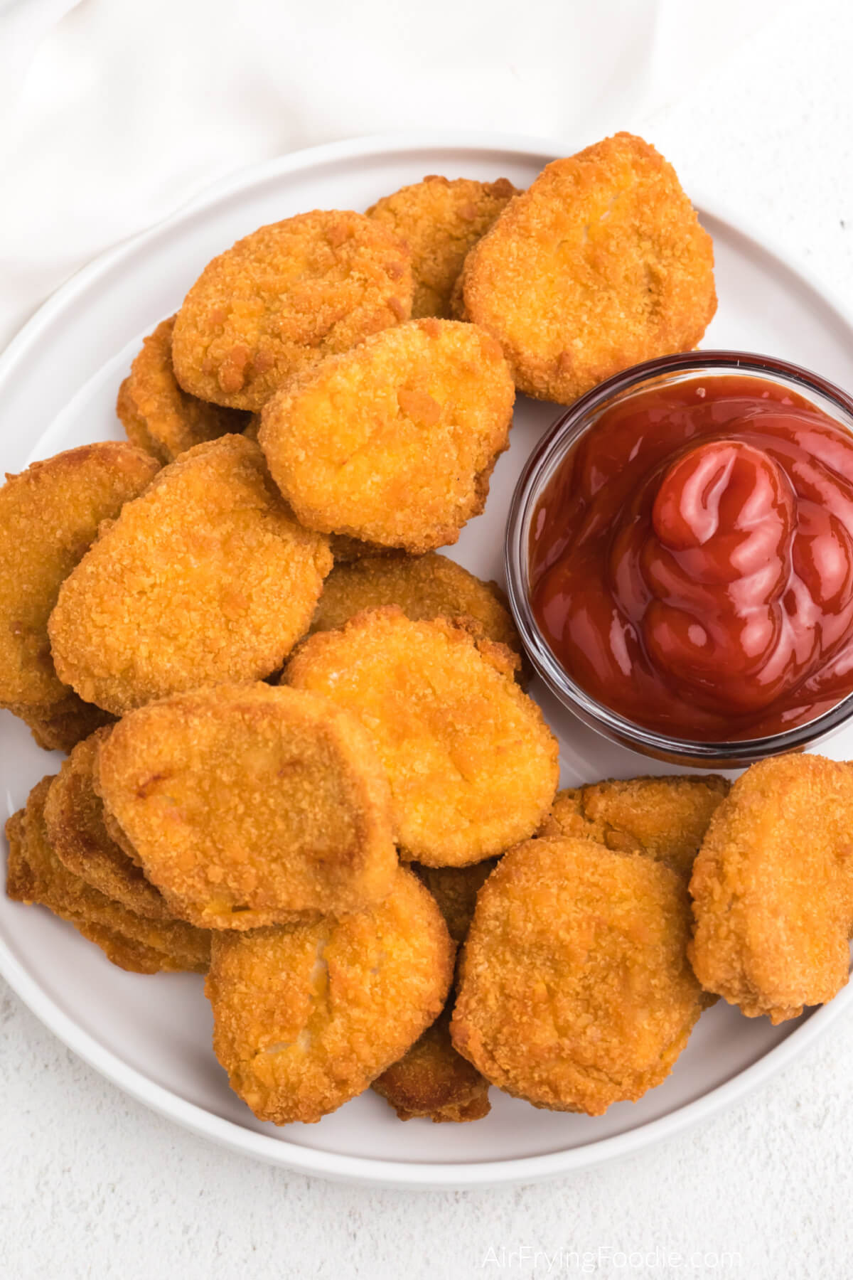 air fryer chicken nuggets fully cooked and served on a white plate with a side of ketchup. 