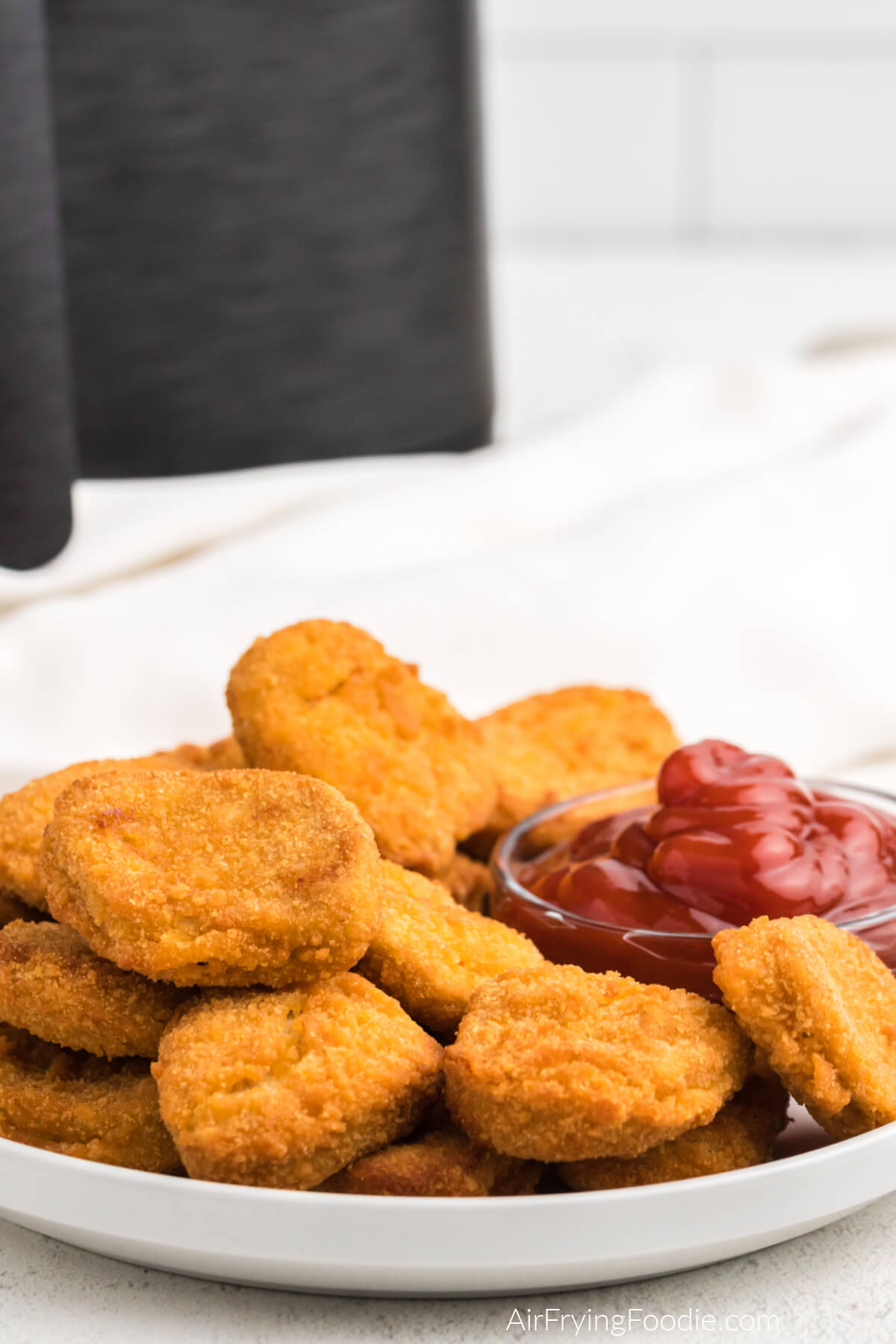 Crispy air fried chicken nuggets on a white plate with a small size of ketchup for dipping. 