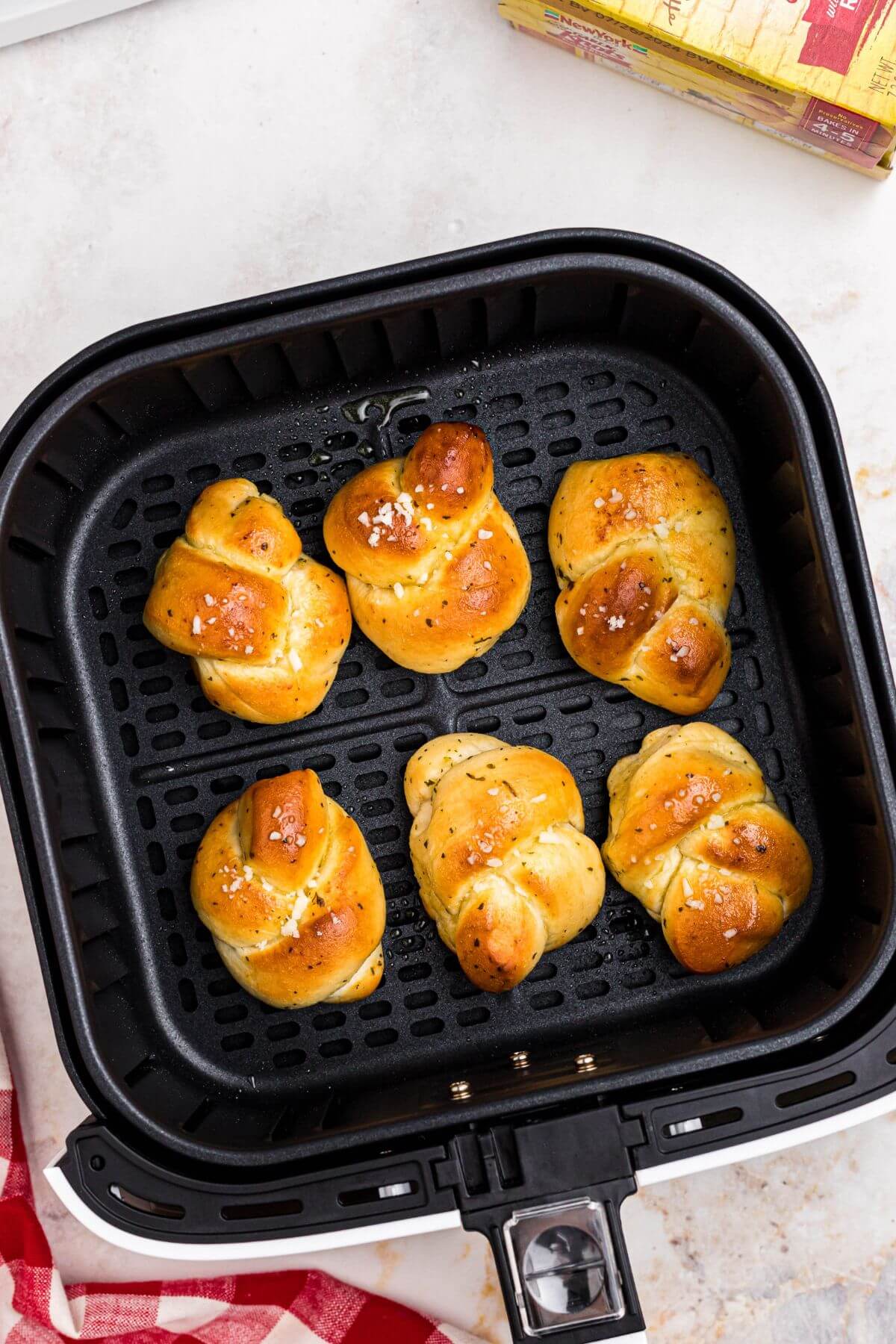Golden garlic knots topped with olive oil and cheese in the air fryer basket. 