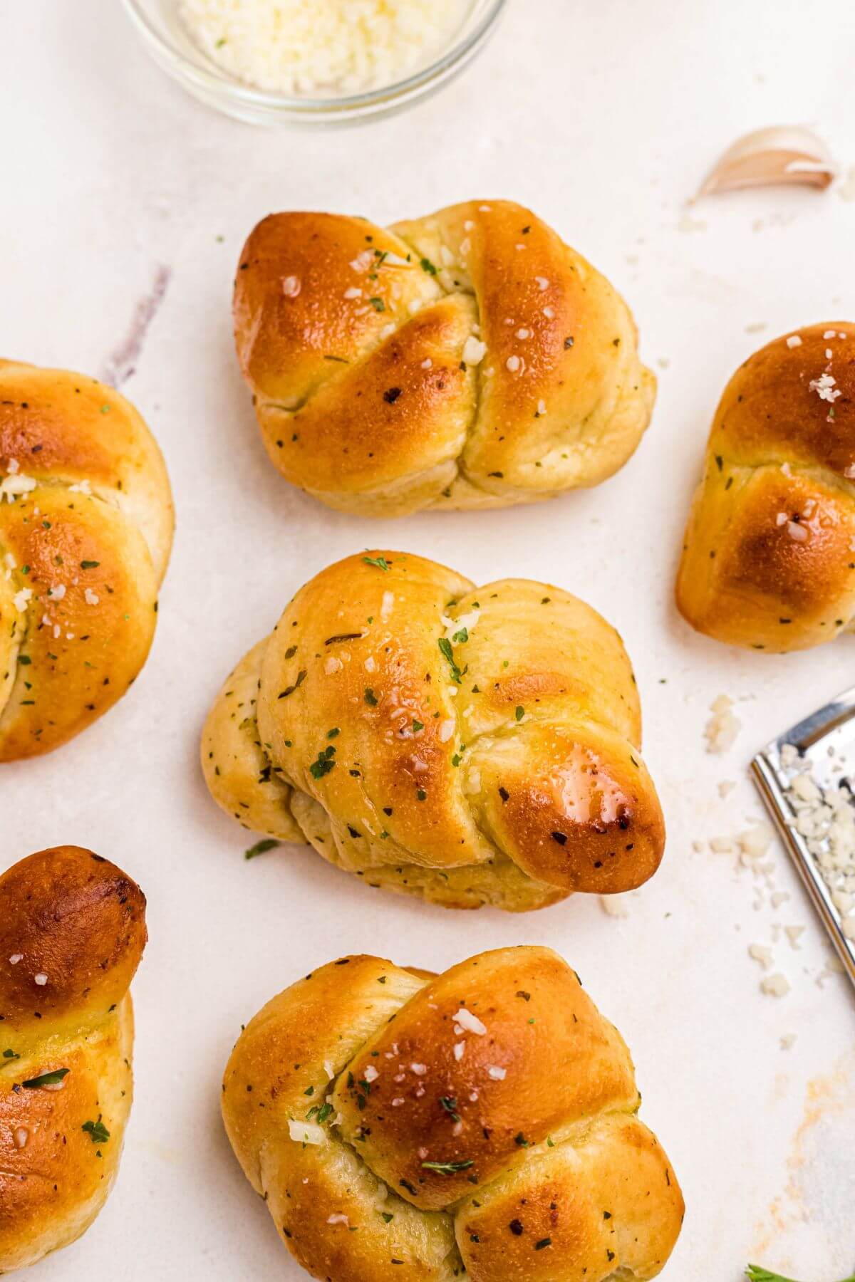 Golden garlic knots brushed with olive oil and shredded cheese on a marble table.