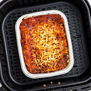 Juicy lasagna in a small tray in the air fryer basket.