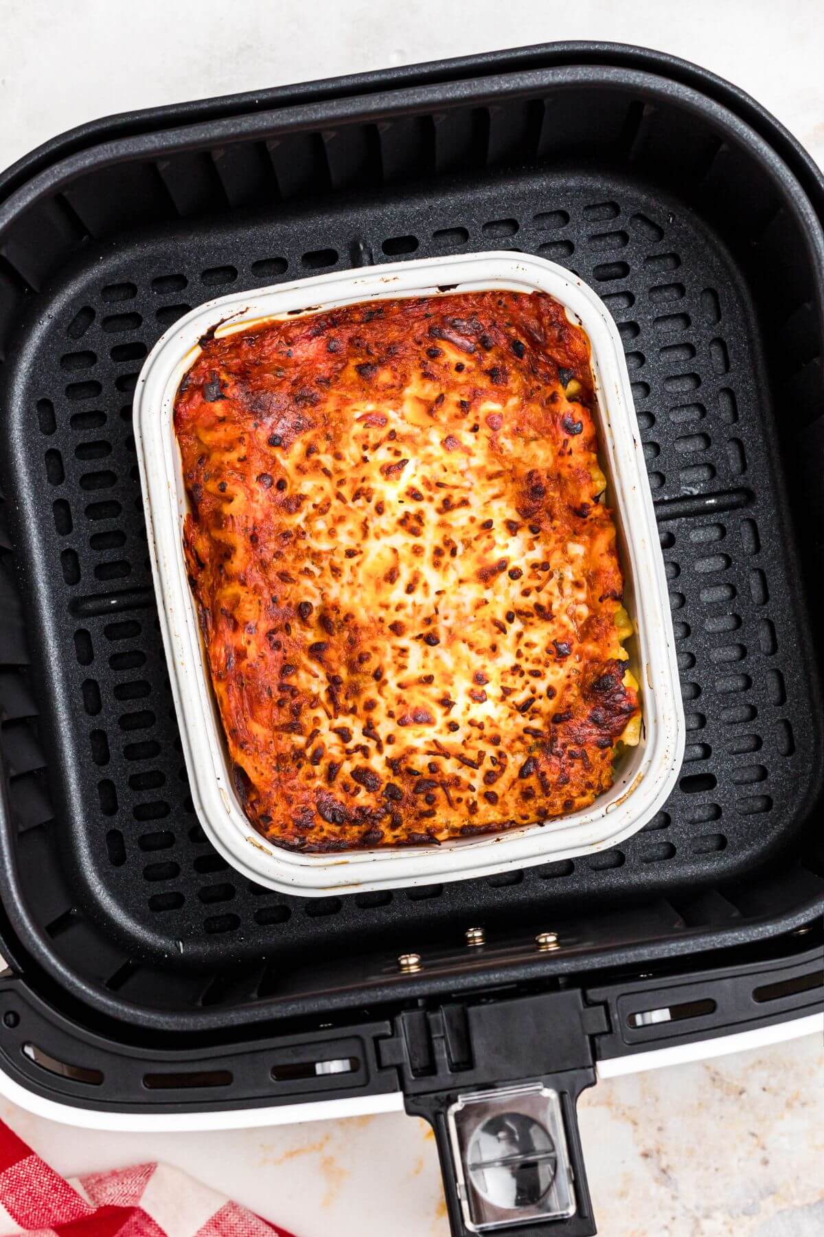 golden orange lasagna in a small tray in the air fryer basket after being cooked. 