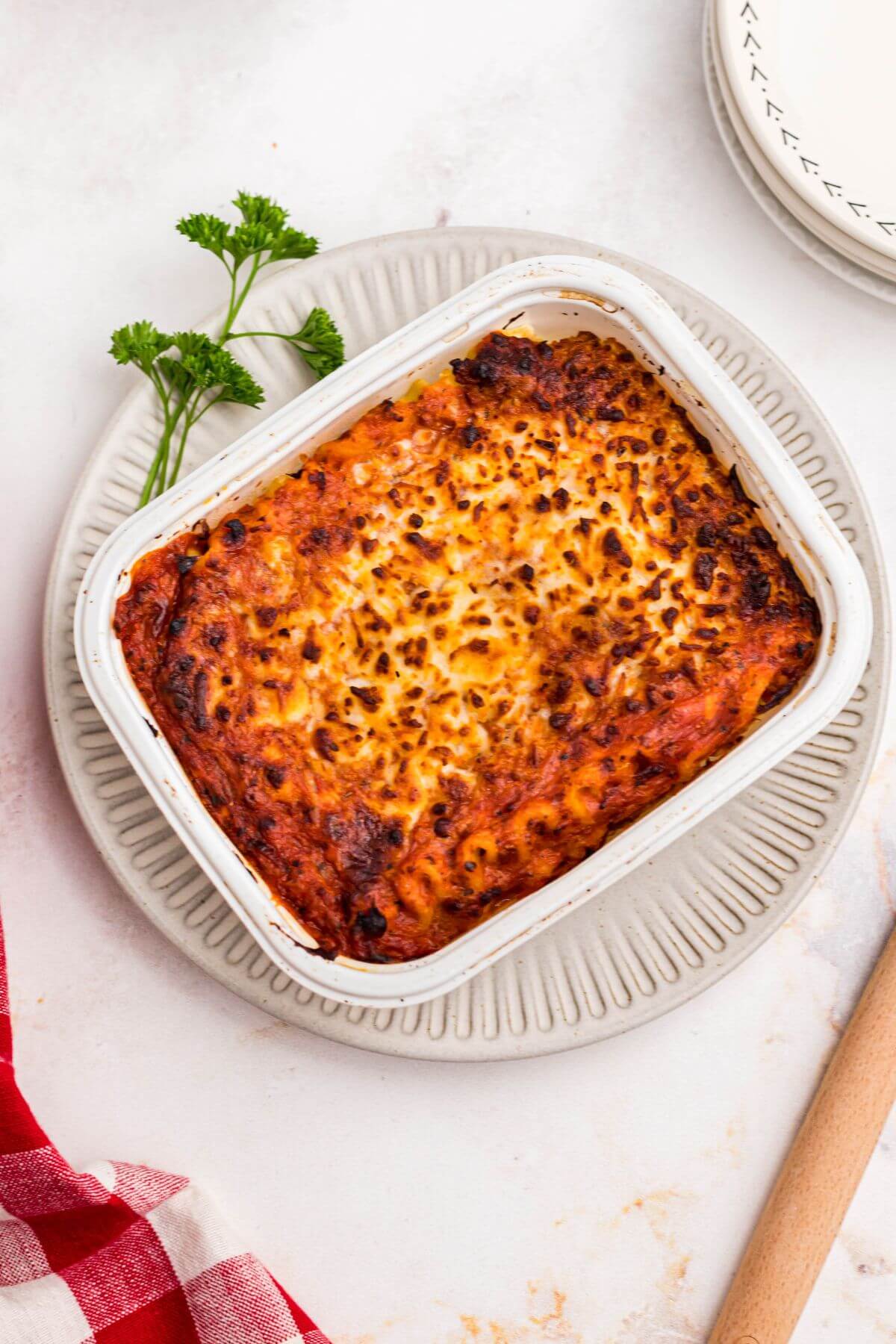 Juicy lasagna in a small tray on a white plate garnished with parsley. 