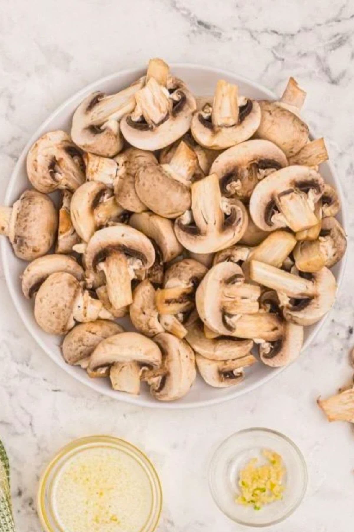 White mushrooms being sliced and placed in a large clear glass bowl. 