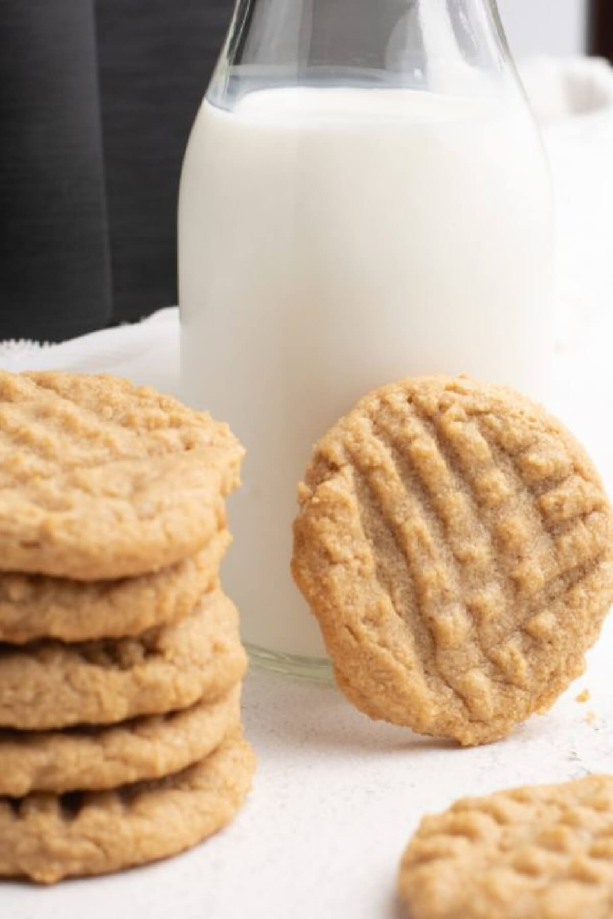 Close up photo of peanut butter cookies made in the air fryer, propped up on a glass of milk. 