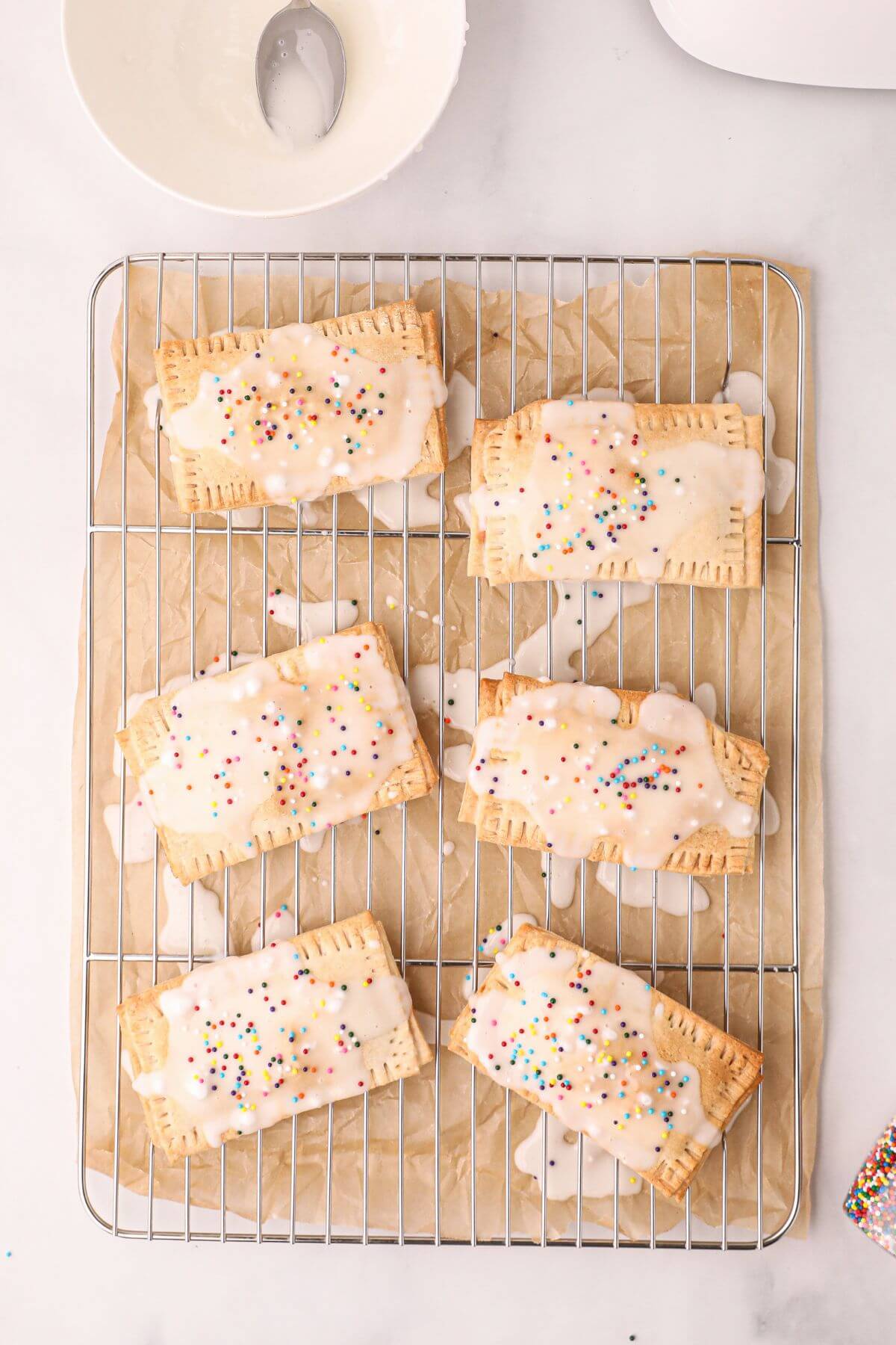 Golden pastries drizzled with white glaze and sprinkles on a cooling rack. 