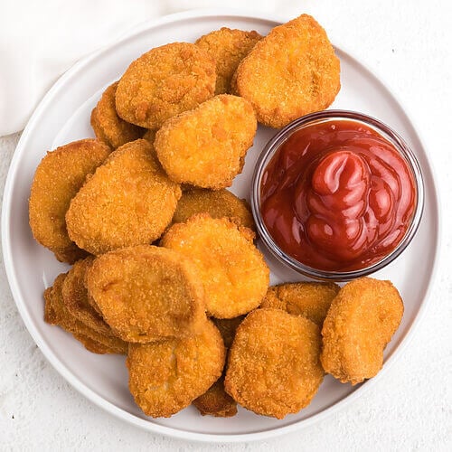 overhead photo of chicken nuggets made in the air fryer served on a white plate with ketchup.