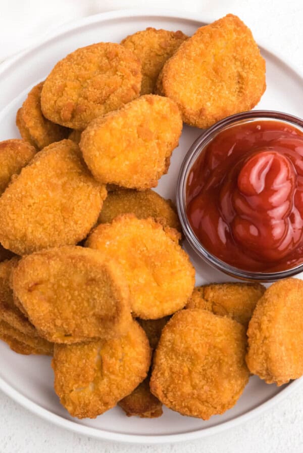 overhead photo of chicken nuggets made in the air fryer served on a white plate with ketchup.