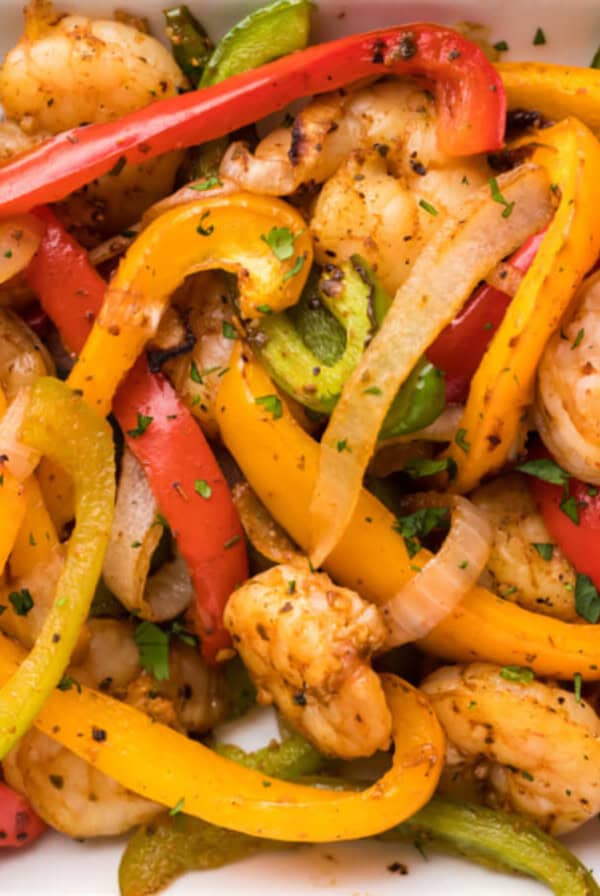 shrimp fajitas mixture with bell peppers, onion, and shrimp, with sliced avocados on a white serving plate.