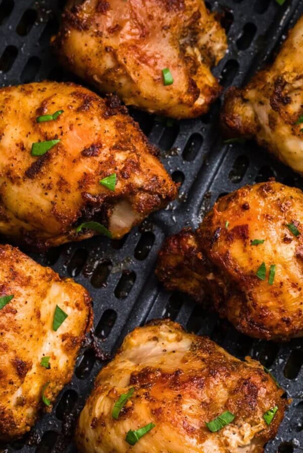 olden brown crispy chicken thighs in the air fryer basket after being cooked.