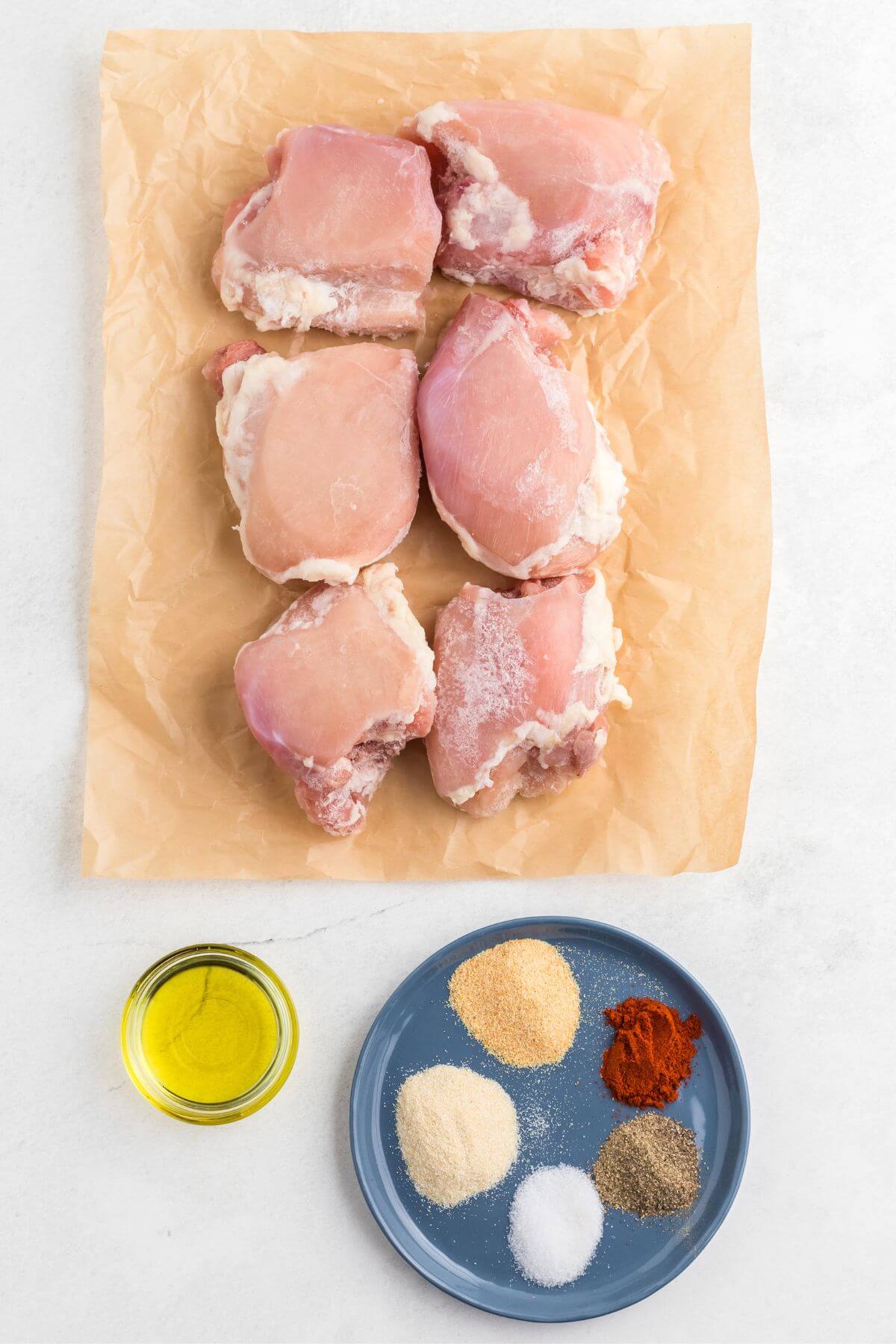 Uncooked chicken thighs, seasonings, and olive oil measured out on a table. 