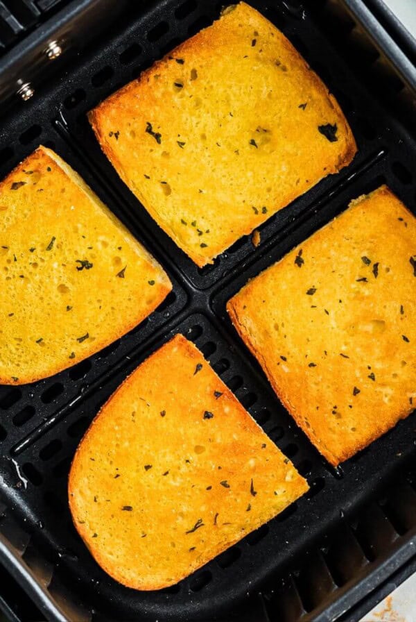 Golden crispy buttered garlic bread in the air fryer basket after being cooked.