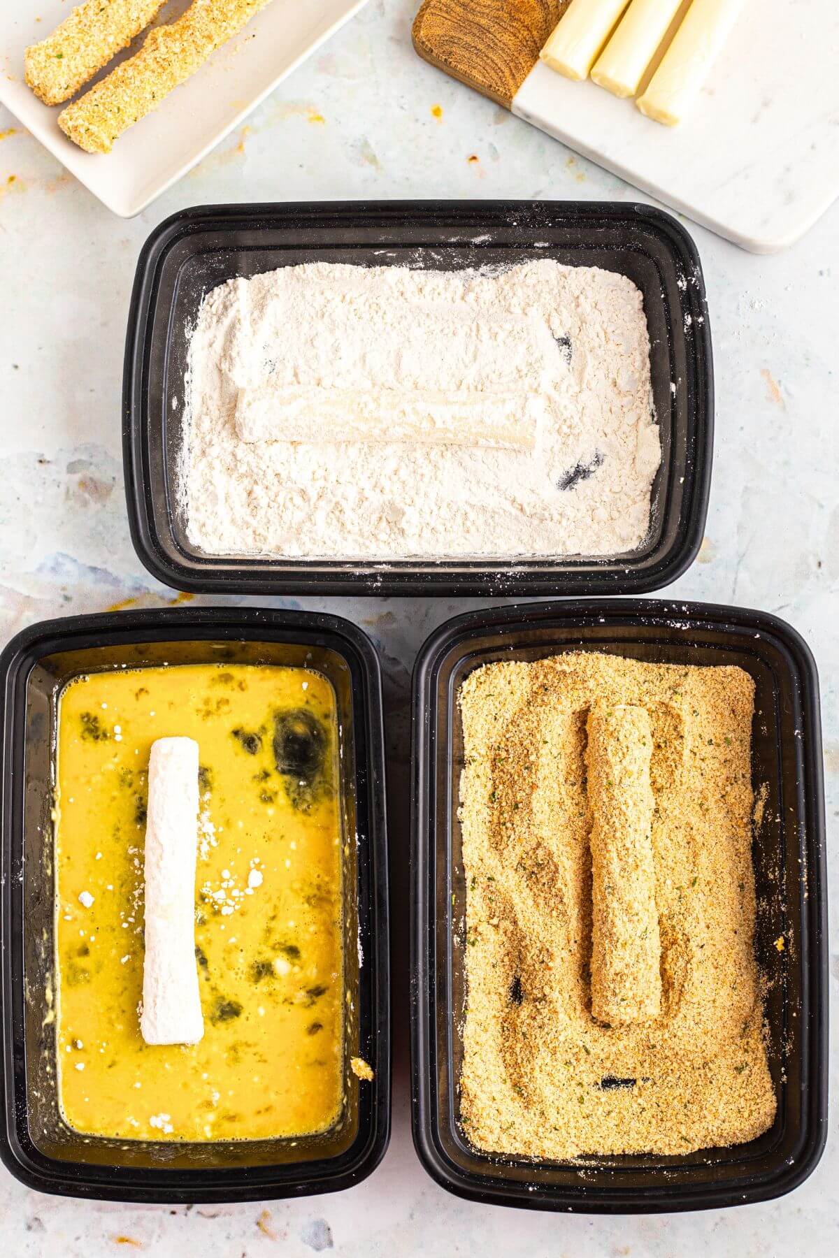 Frozen cheese sticks being dredged in flour, then egg, then breadcrumbs. 